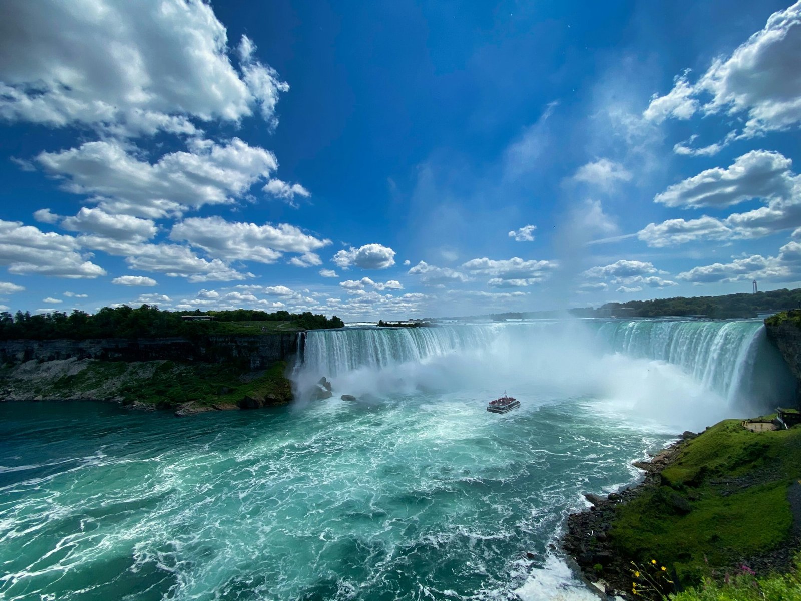 Horseshoe Falls in Niagara Falls, Ontario, under a blue sky with mist rising from the river
